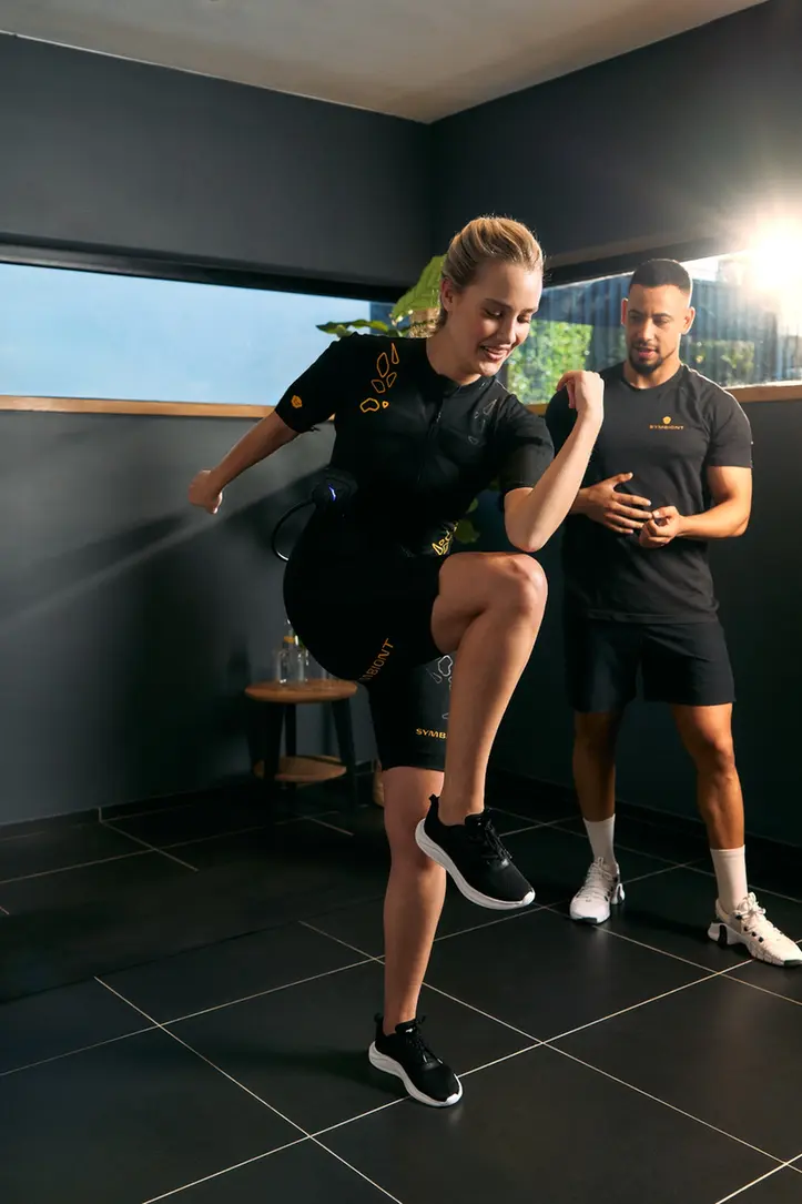 A personal trainer guides a client wearing a SYMBIONT EMS suit during a trial session at a local EMS studio. Experience personalized training, individual support, and motivation in your EMS trial session.