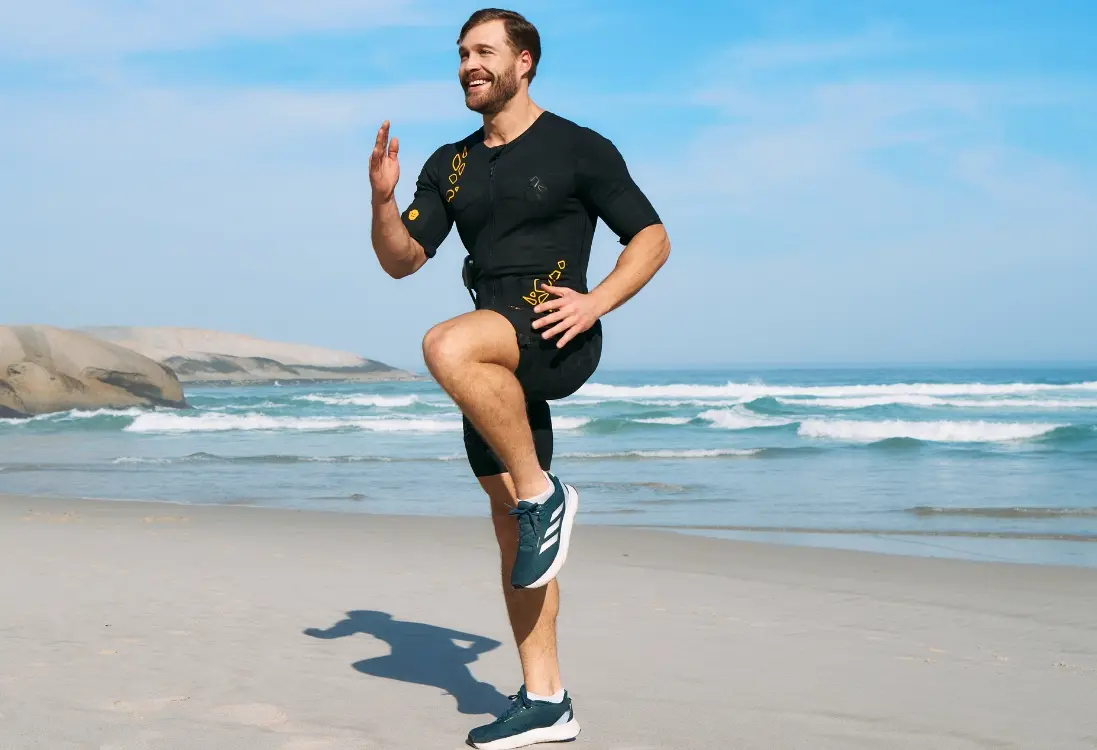 Een man in een EMS-pak traint buiten op het strand en voert een effectieve en intensieve workout uit om vet te verminderen en gewichtsverlies te ondersteunen met EMS.